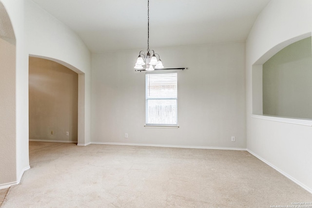 empty room with a notable chandelier, light colored carpet, and lofted ceiling