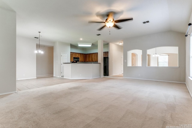 unfurnished living room featuring ceiling fan with notable chandelier, light colored carpet, and vaulted ceiling