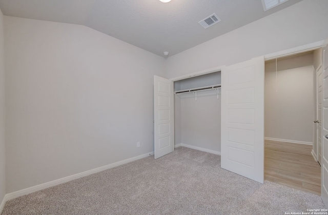 unfurnished bedroom featuring lofted ceiling, a closet, and light carpet