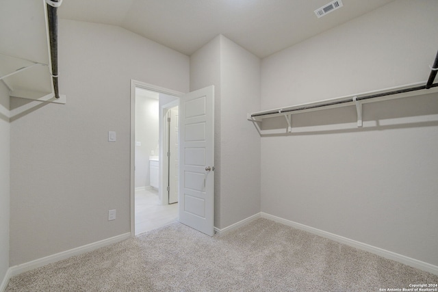 walk in closet with vaulted ceiling and light colored carpet