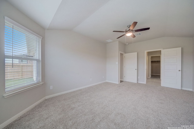 unfurnished bedroom featuring light carpet, ceiling fan, a closet, vaulted ceiling, and a walk in closet