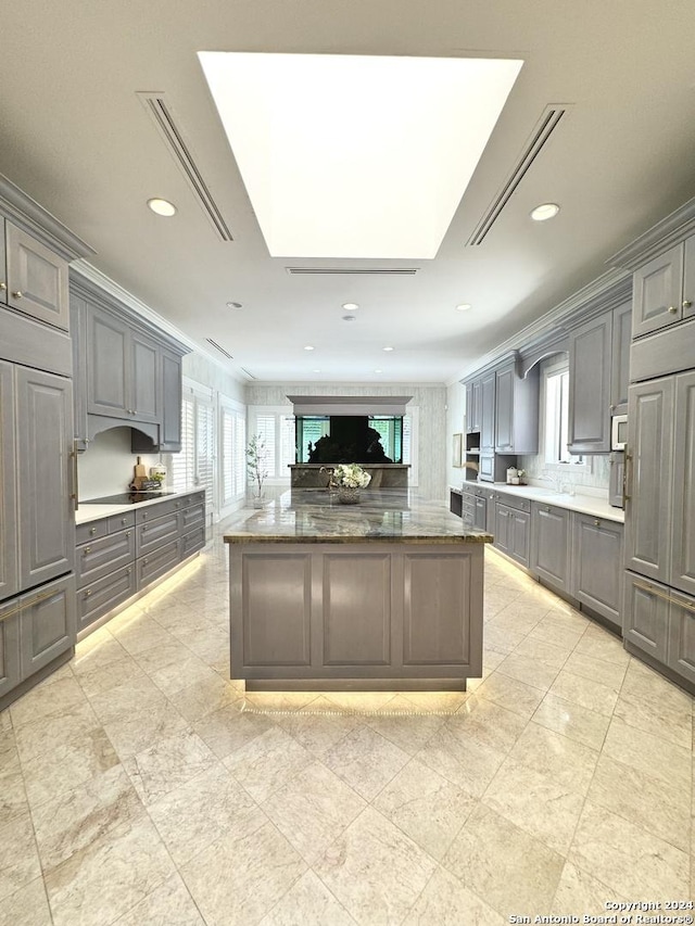 kitchen featuring dark stone countertops, black electric stovetop, gray cabinetry, and a skylight