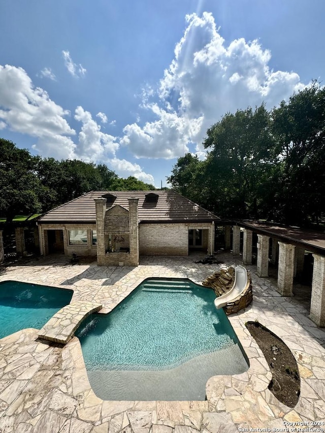 view of pool with a water slide, a fireplace, and a patio area