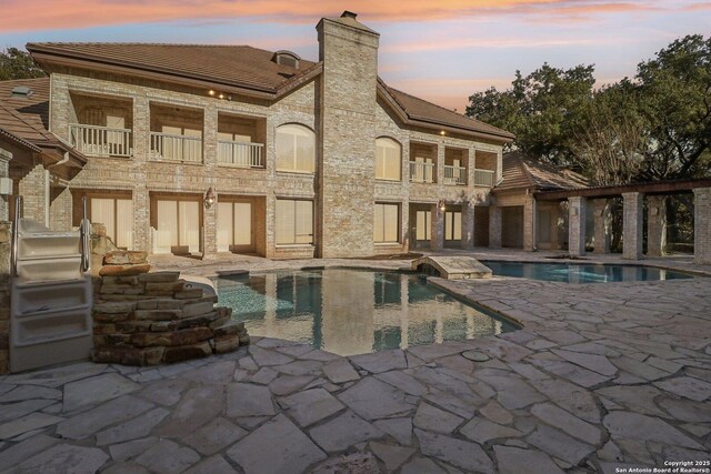 back house at dusk featuring a patio area and a balcony