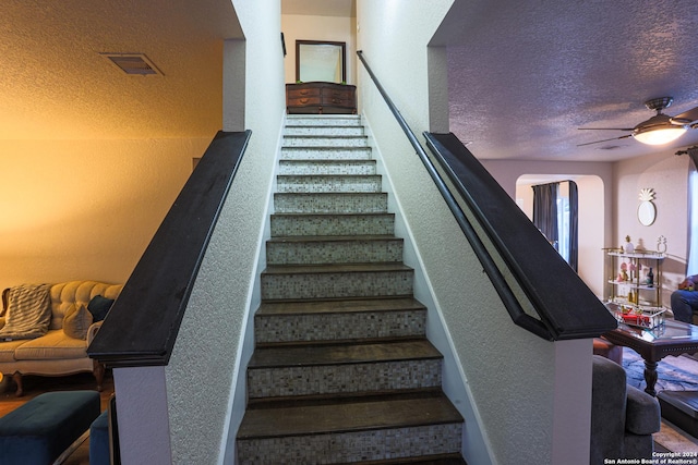 stairway with ceiling fan and a textured ceiling