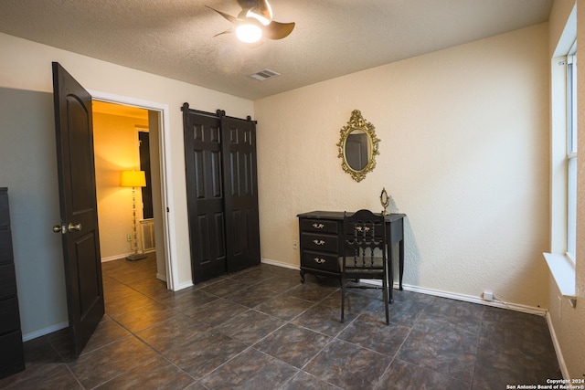 bedroom featuring ceiling fan, a barn door, and a textured ceiling