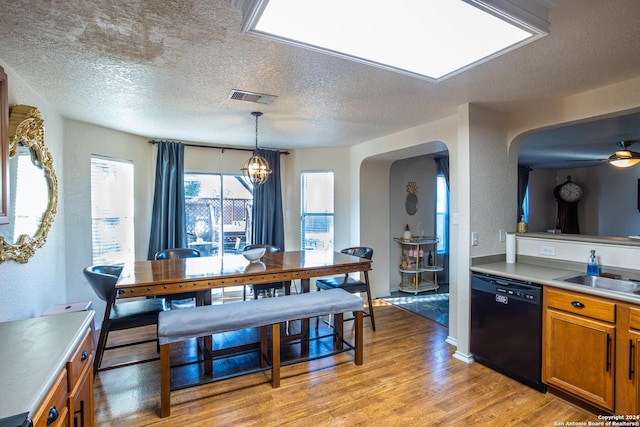 kitchen featuring dishwasher, sink, light wood-type flooring, hanging light fixtures, and an inviting chandelier