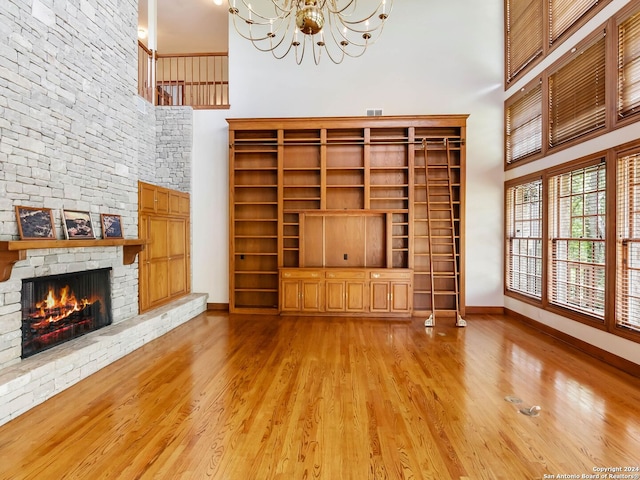 unfurnished living room featuring a stone fireplace, a notable chandelier, light wood-type flooring, and a high ceiling