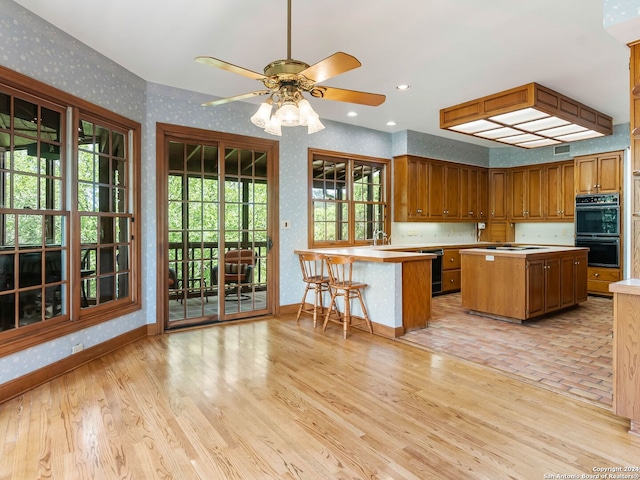 kitchen with light hardwood / wood-style floors, black appliances, ceiling fan, and a kitchen breakfast bar