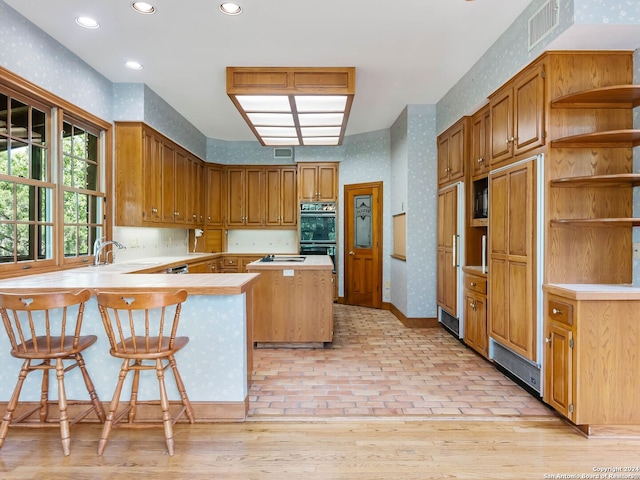 kitchen with stovetop, black double oven, a center island, a breakfast bar, and kitchen peninsula