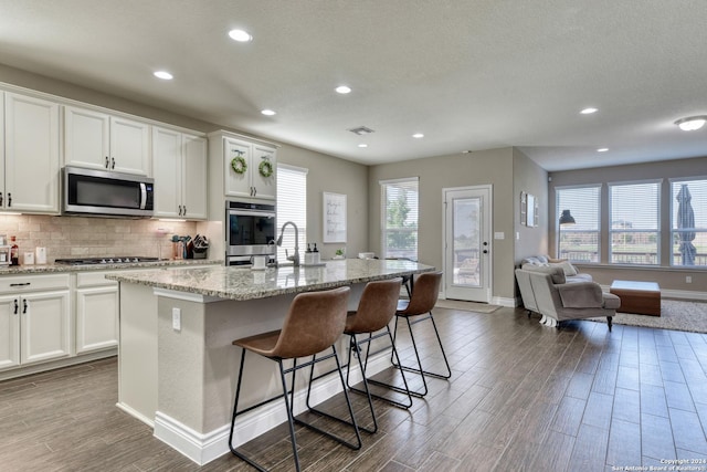 kitchen with stainless steel appliances, light stone counters, a breakfast bar area, a kitchen island with sink, and white cabinets