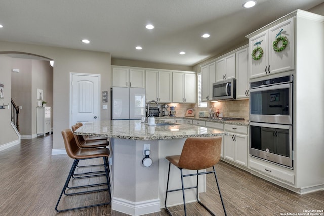 kitchen with light stone counters, white cabinetry, an island with sink, and appliances with stainless steel finishes