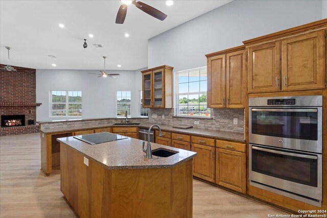 kitchen with double oven, electric stovetop, a center island with sink, and sink