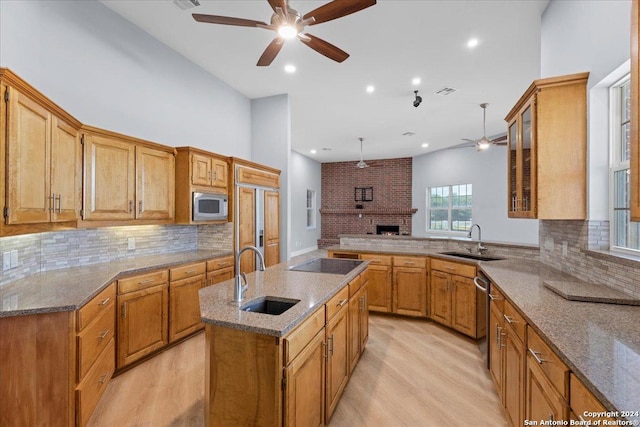 kitchen featuring a kitchen island with sink, black electric stovetop, sink, built in microwave, and light hardwood / wood-style floors