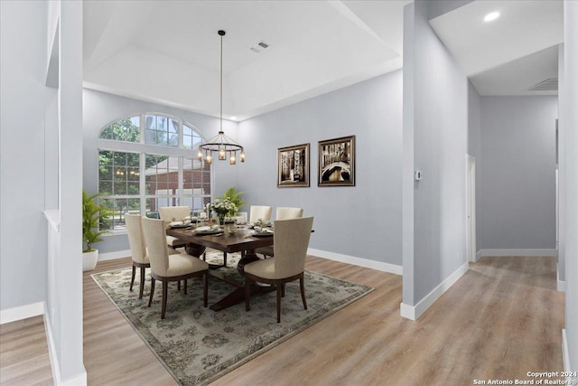 dining space with a high ceiling, an inviting chandelier, light hardwood / wood-style flooring, and a raised ceiling