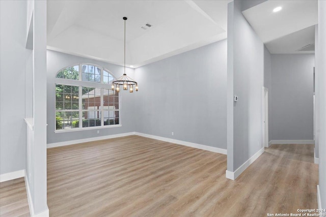 unfurnished dining area featuring light wood-type flooring, a raised ceiling, and a notable chandelier