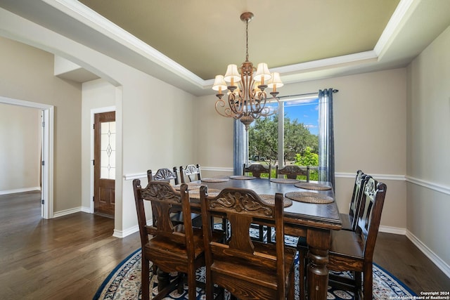 dining space featuring dark wood-type flooring, a raised ceiling, and a chandelier