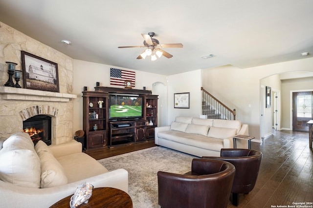 living room with ceiling fan, dark hardwood / wood-style floors, and a stone fireplace