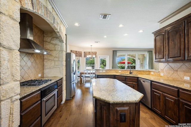 kitchen featuring pendant lighting, sink, wall chimney range hood, appliances with stainless steel finishes, and a kitchen island