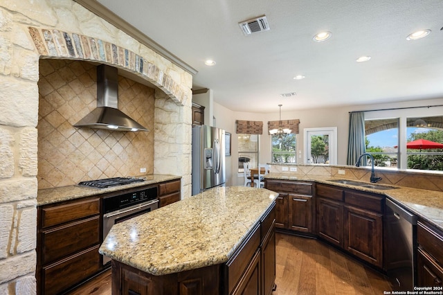 kitchen with appliances with stainless steel finishes, sink, hanging light fixtures, a center island, and wall chimney exhaust hood