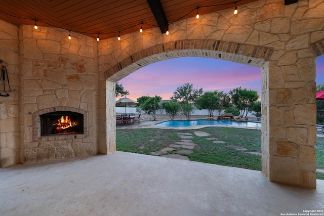 pool at dusk with a patio area and an outdoor stone fireplace