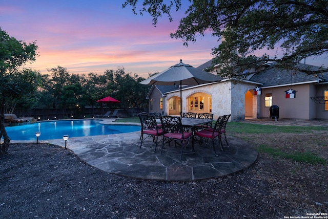 pool at dusk with a grill and a patio