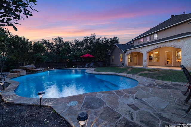 pool at dusk with a patio and pool water feature