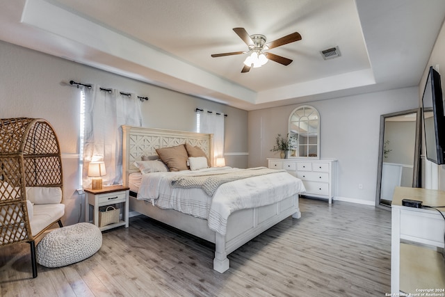 bedroom with multiple windows, wood-type flooring, ceiling fan, and a raised ceiling