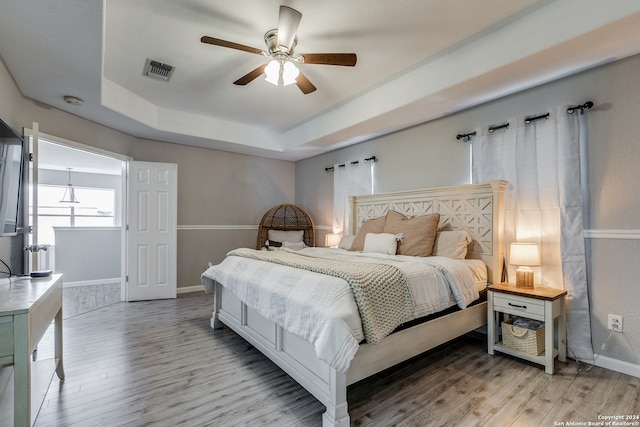 bedroom with ceiling fan, a raised ceiling, and light hardwood / wood-style floors