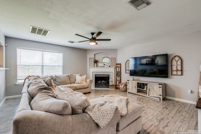 living room with a fireplace, light hardwood / wood-style floors, a textured ceiling, and ceiling fan