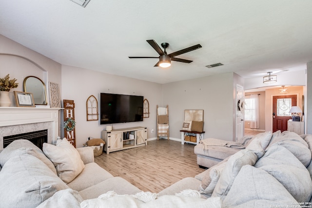 living room featuring light hardwood / wood-style flooring, a tile fireplace, and ceiling fan