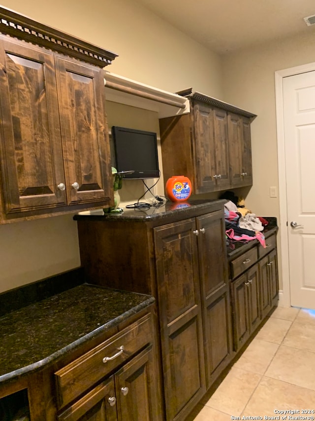 kitchen featuring dark brown cabinetry, dark stone countertops, and light tile patterned floors