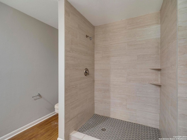 bathroom with tiled shower, toilet, and wood-type flooring