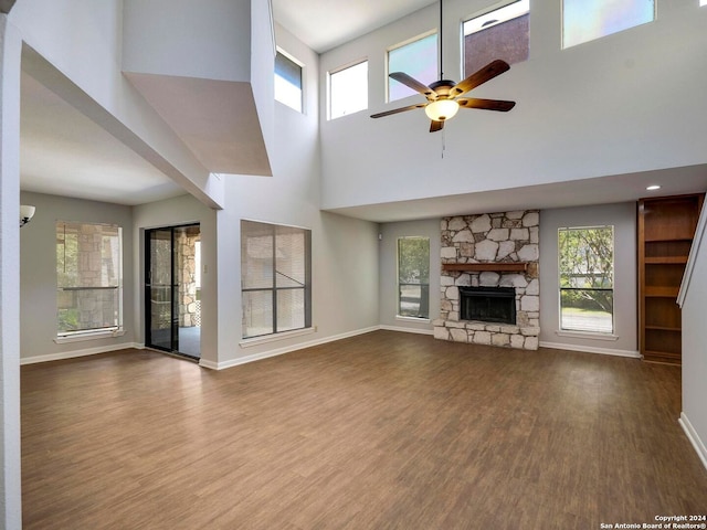 unfurnished living room with a fireplace, ceiling fan, hardwood / wood-style floors, and a high ceiling