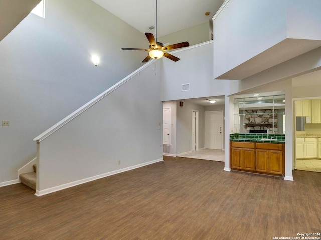 unfurnished living room with sink, a high ceiling, hardwood / wood-style flooring, and ceiling fan