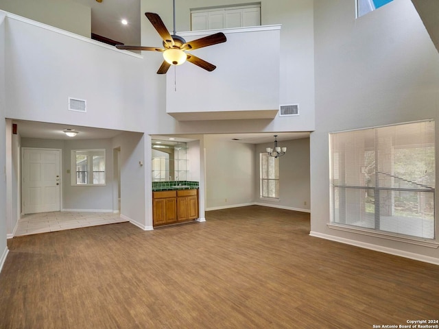 unfurnished living room with a wealth of natural light, hardwood / wood-style floors, ceiling fan with notable chandelier, and a towering ceiling