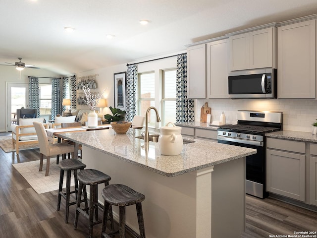 kitchen with light stone counters, a center island with sink, appliances with stainless steel finishes, and decorative backsplash