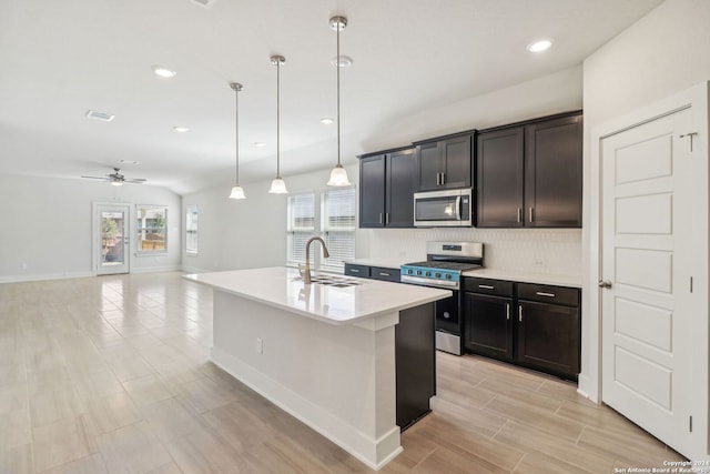 kitchen featuring a center island with sink, sink, backsplash, appliances with stainless steel finishes, and decorative light fixtures