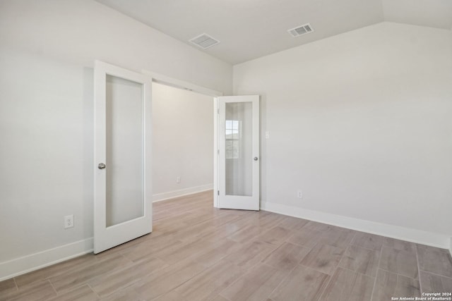 unfurnished room with french doors, light hardwood / wood-style flooring, and vaulted ceiling