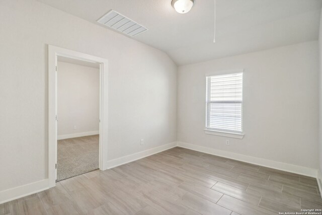 spare room with light wood-type flooring and lofted ceiling