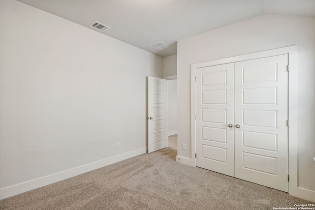 unfurnished bedroom with light colored carpet, a closet, and vaulted ceiling