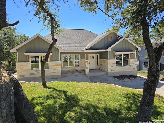 craftsman inspired home with stone siding, a shingled roof, a front lawn, and board and batten siding