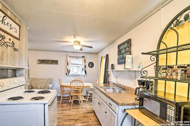 kitchen with black microwave, electric range, a sink, white cabinets, and light wood-type flooring