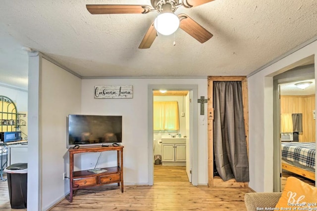 living room with a textured ceiling, light wood finished floors, a ceiling fan, and baseboards