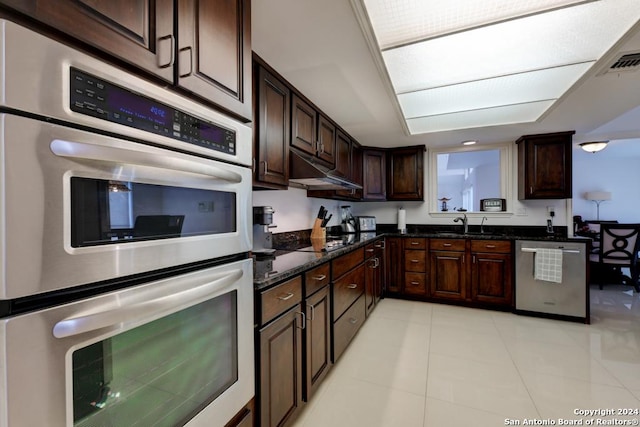 kitchen with light tile patterned flooring, stainless steel appliances, dark brown cabinets, and dark stone counters