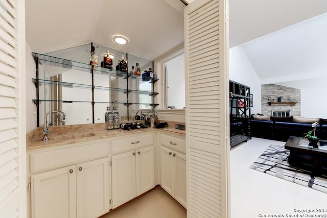 bar with a brick fireplace, sink, light tile patterned flooring, and vaulted ceiling