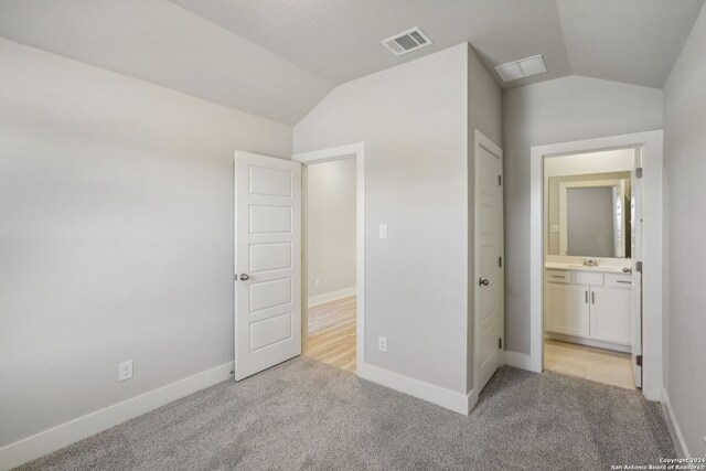 unfurnished bedroom with sink, connected bathroom, light carpet, and vaulted ceiling