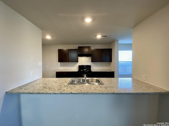 kitchen featuring kitchen peninsula, light stone countertops, sink, and dark brown cabinets