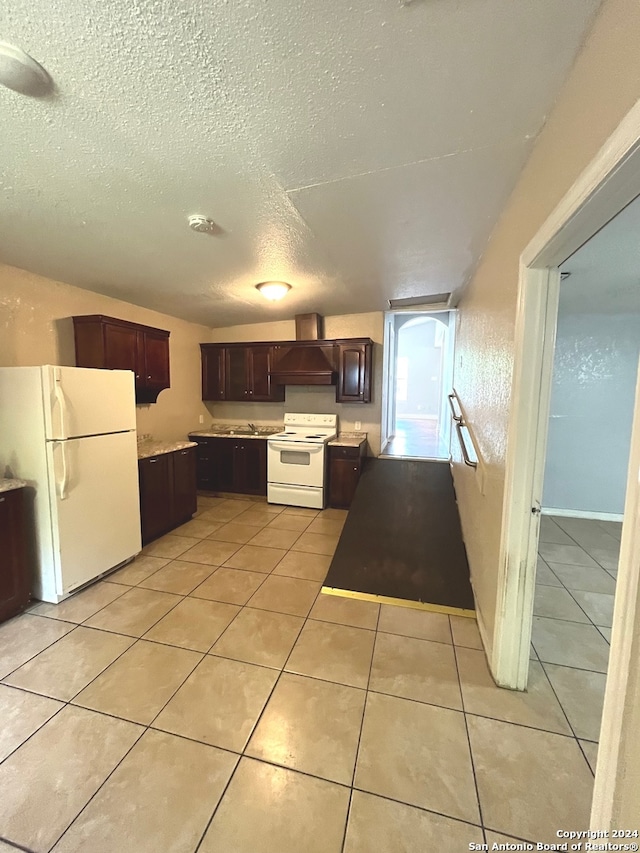 kitchen with dark brown cabinets, white appliances, light tile patterned floors, a textured ceiling, and premium range hood