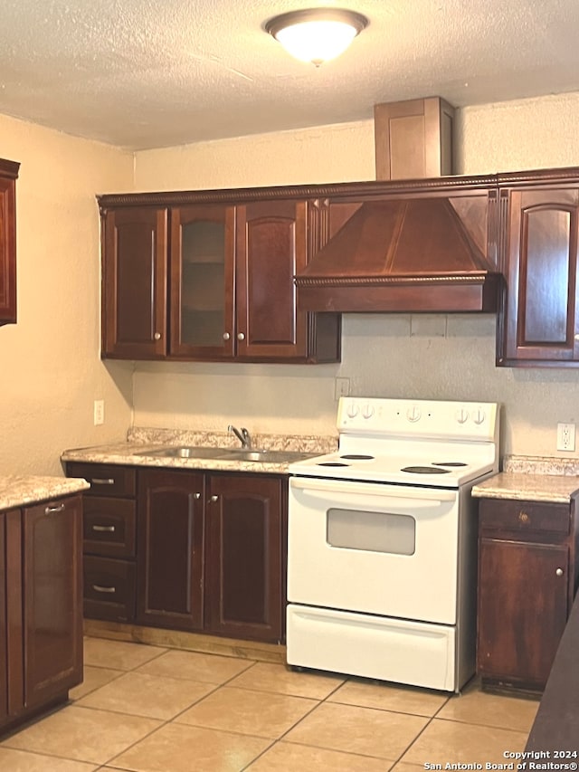 kitchen with light tile patterned floors, a textured ceiling, white electric range, premium range hood, and dark brown cabinetry